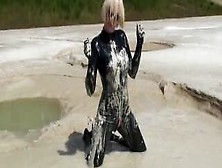 Super Hot Blond Girl In Black Latex Catsuit + High Heels And Sunglasses Bathes In The Mud - Mud Bath